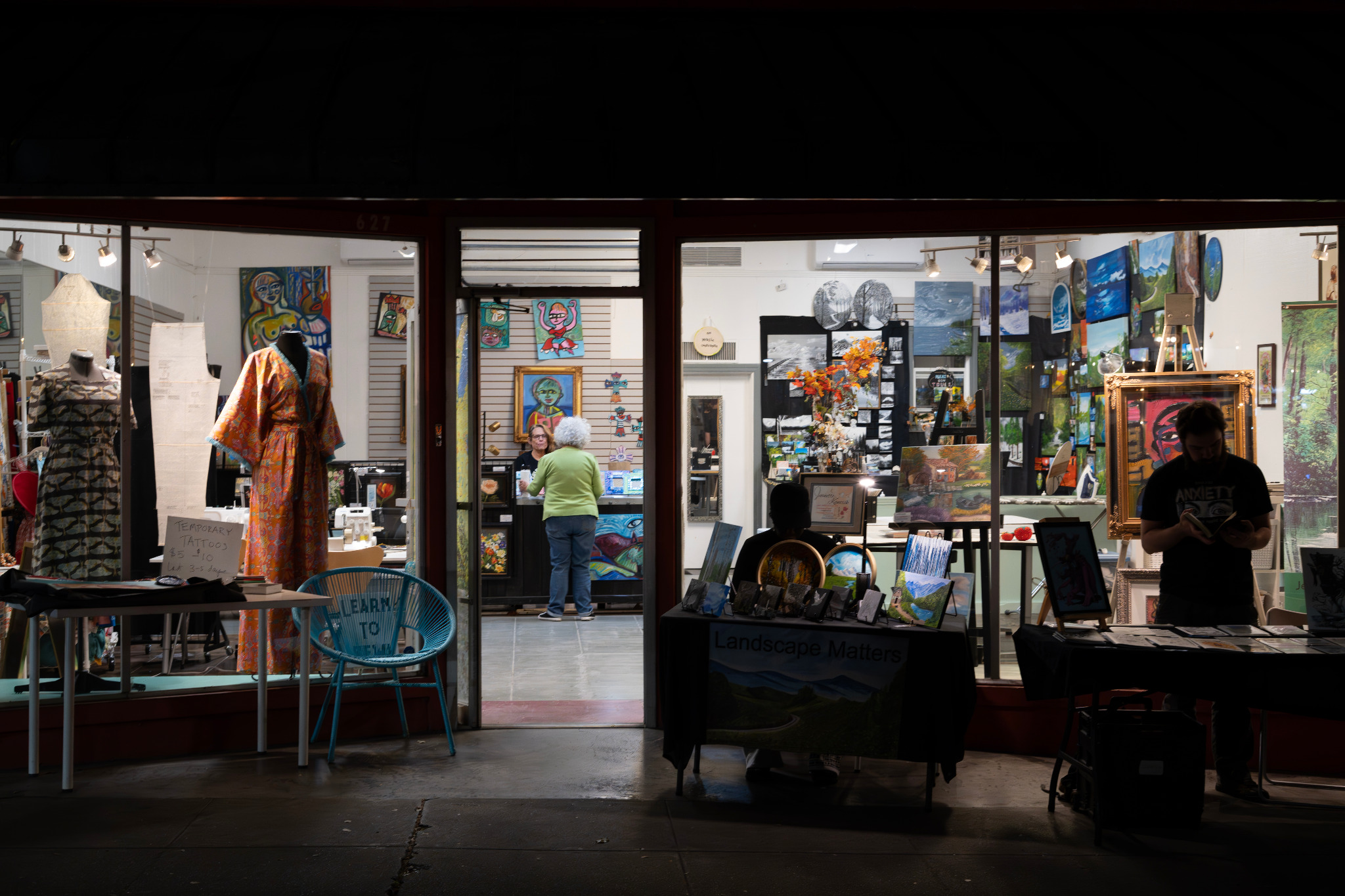 A lit storefront displaying artwork and local retail activity.